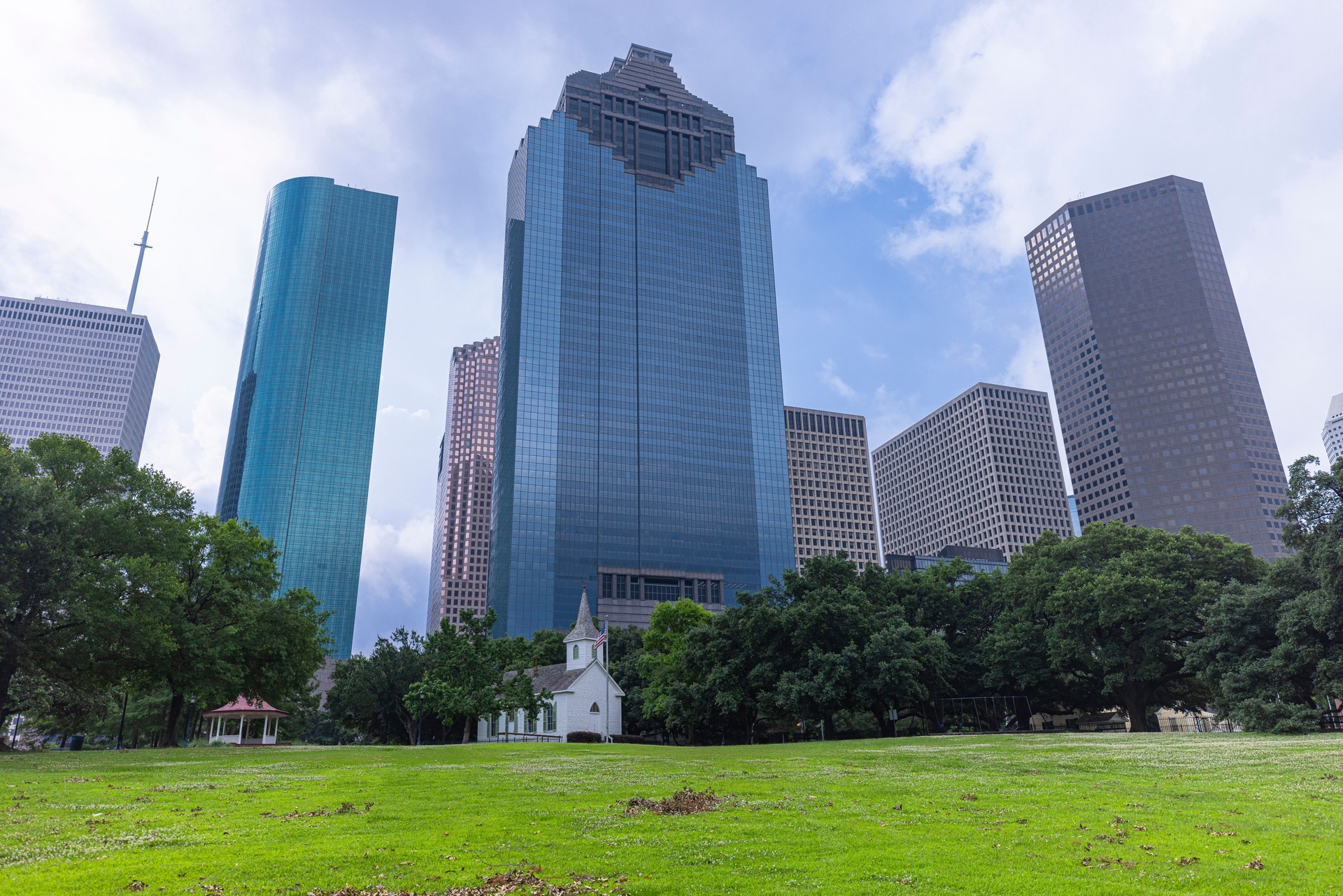 Historic St.John Church stands amid urban growth. White church and lush trees contrast with Houston's towering skyscrapers in Sam Houston Park in Texas