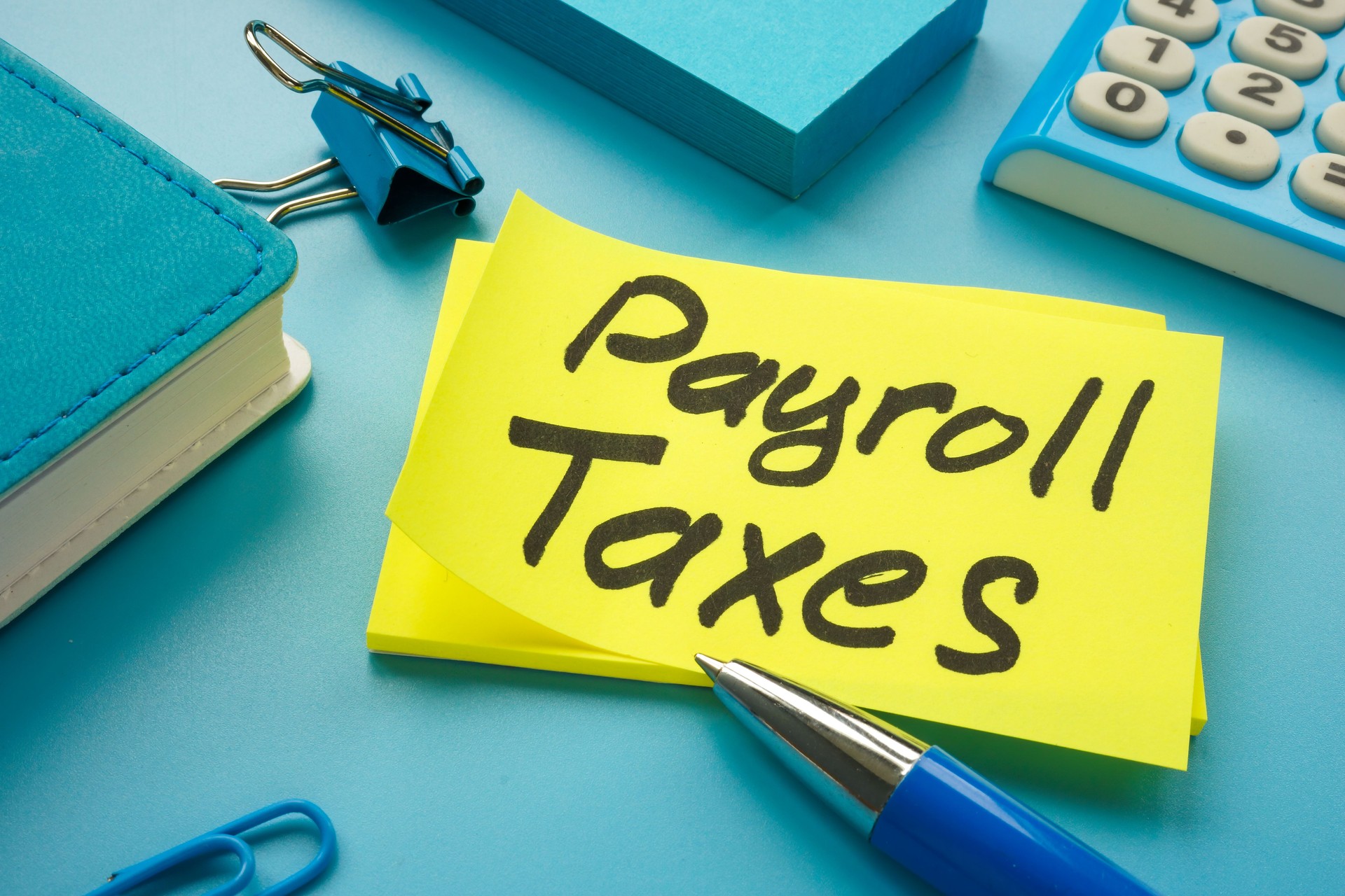 Payroll taxes on the yellow memo stick and calculator.